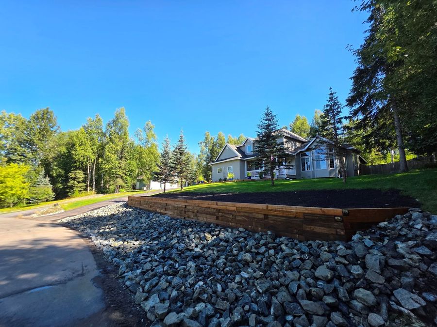 Stone retaining wall on a brown hillside with leafless trees and patches of snow under a blue sky
