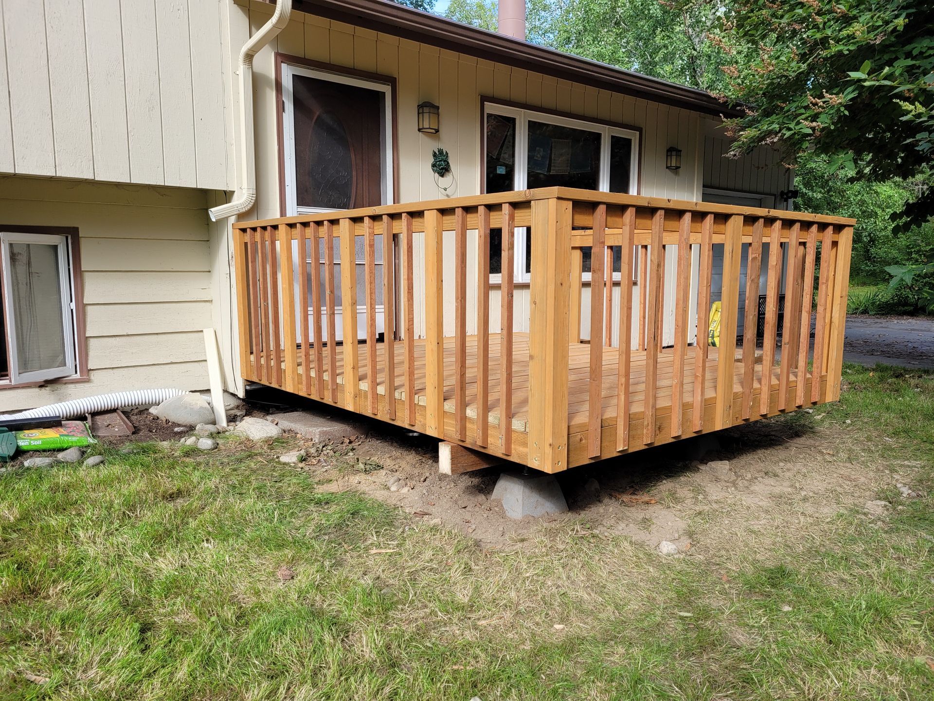 Wooden deck and railing attached to a beige house beside a grassy yard.