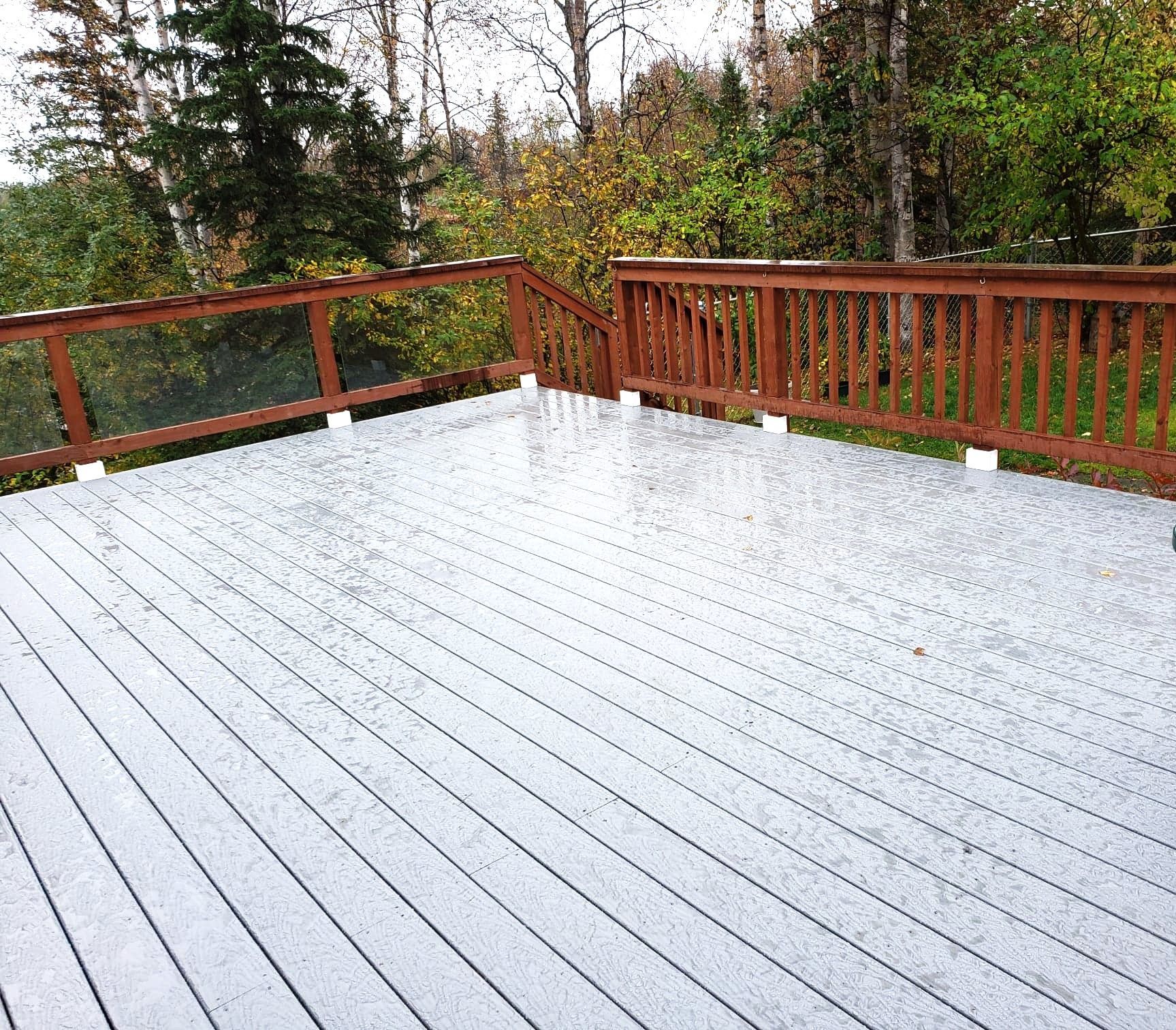 Snow-covered wooden deck with red railing and trees in the background