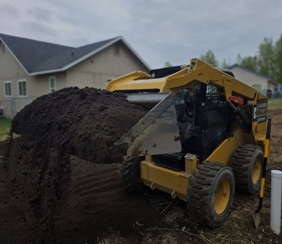 Yellow skid steer dumping a pile of dark soil on a suburban driveway