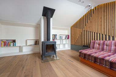 Modern living room with wood stove, hardwood floors, built-in shelves, and a patterned sofa