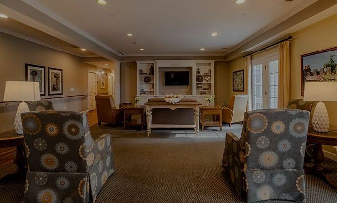 Cozy living room with two patterned armchairs, a fireplace, and large windows letting in daylight