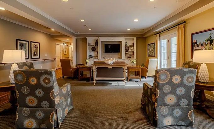 Elegant living room with patterned armchairs, fireplace, windows, and a desk at the back.