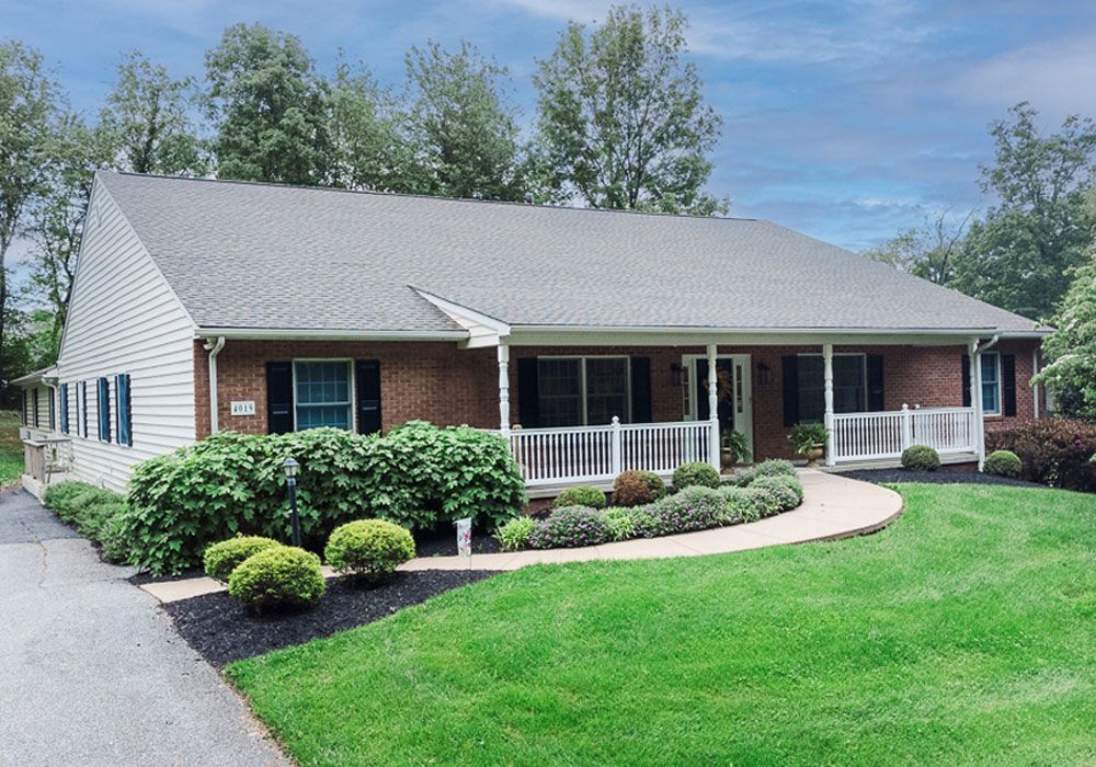 Suburban single-story house with gray siding, front porch, manicured lawn, and shrubs