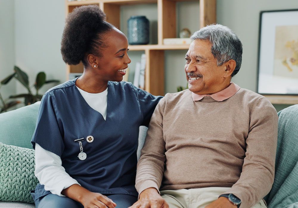 Two people sit on a couch, smiling and talking in a bright living room.