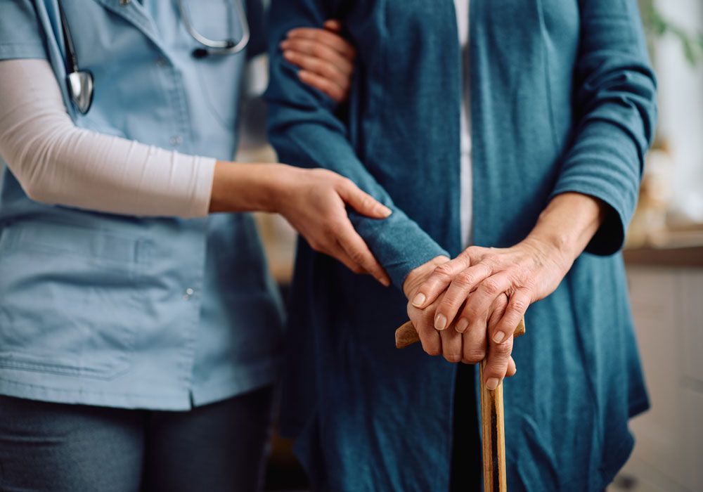 Caregiver holding an elderly person's hand beside a walking cane