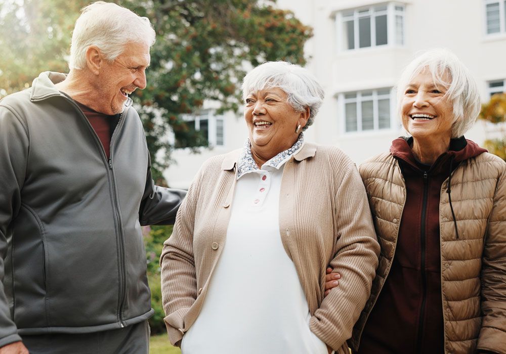 Three older adults smiling and walking together outdoors in a garden