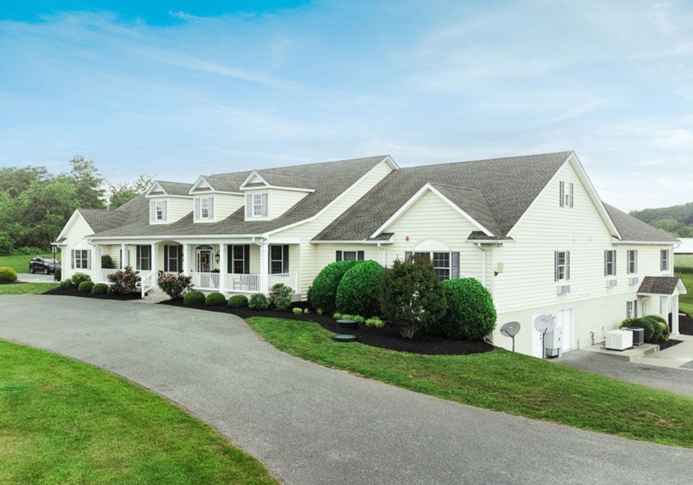 Large white suburban house with curved driveway, and landscaped lawn under a blue sky