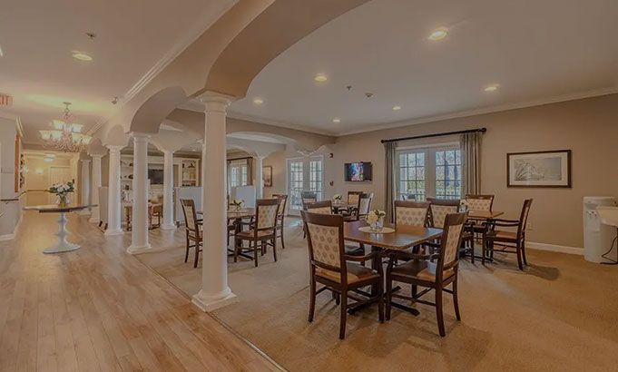Spacious dining room with multiple wooden tables, chairs, columns, and warm recessed lighting