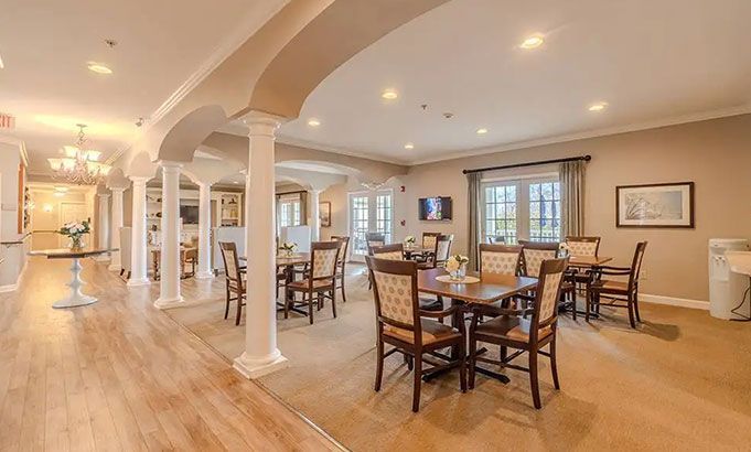 Spacious beige dining and living area with wooden table, chairs, columns, and large windows