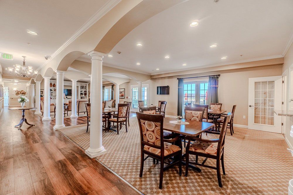 Spacious dining room with patterned chairs, wooden floors, and arched columns under recessed lighting