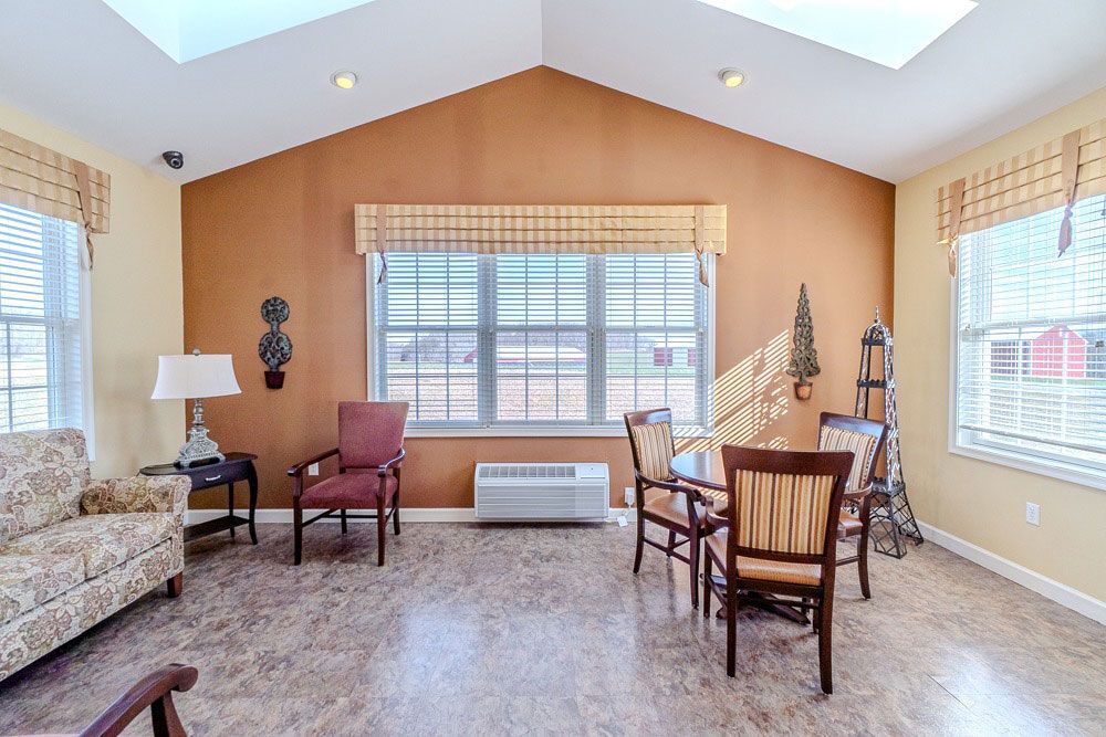 Bright living room with vaulted ceiling, large windows, beige walls, carpet, sofa, chairs, and a table