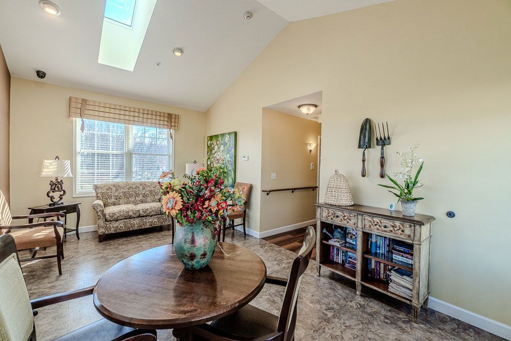 Bright living room with round table, floral centerpiece, sofa, skylight, and bookshelf on the wall
