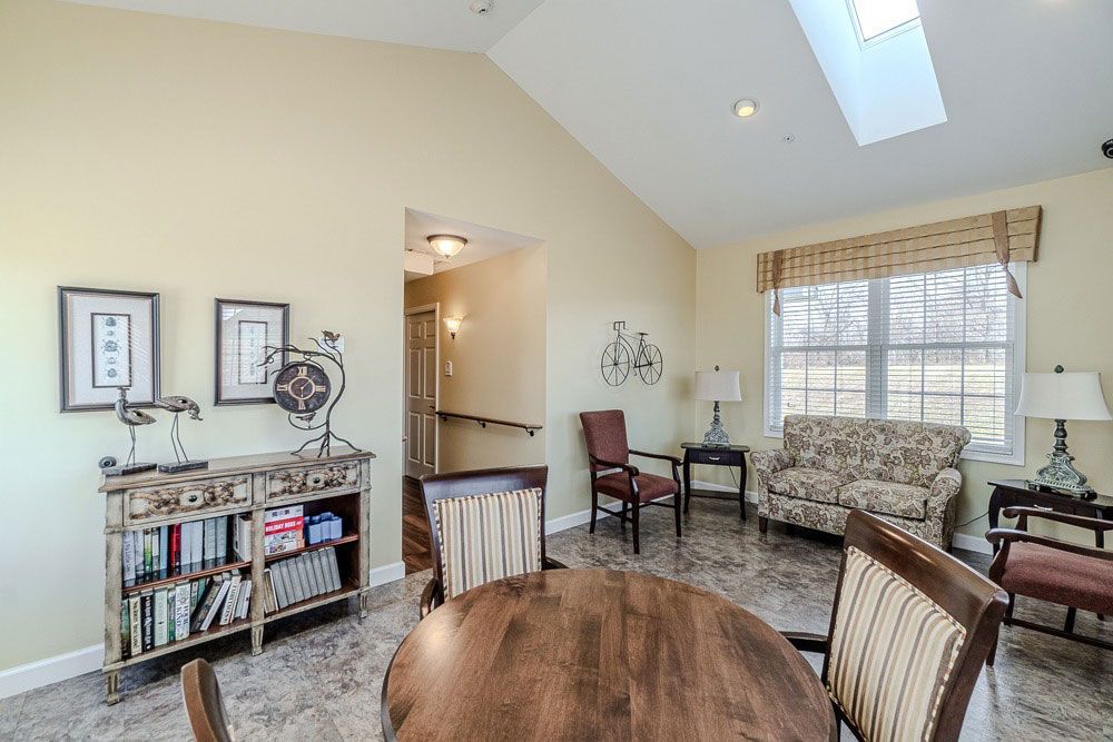 Bright living room with vaulted ceiling, skylight, floral sofa, chairs, and a round table by the window.