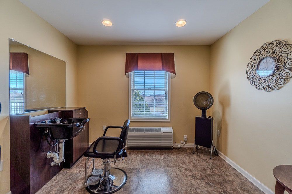 Small home office with desk, chair, window, floor lamp, and wall mirror on beige walls.