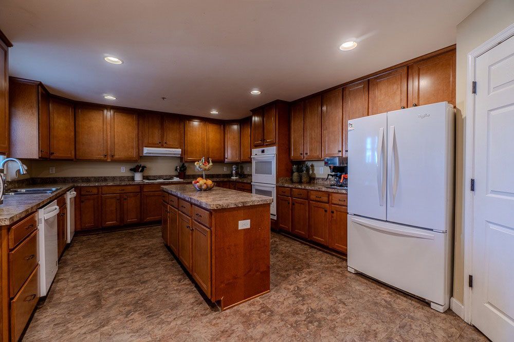 Spacious kitchen with wood cabinets, central island, and white refrigerator on a tiled floor.