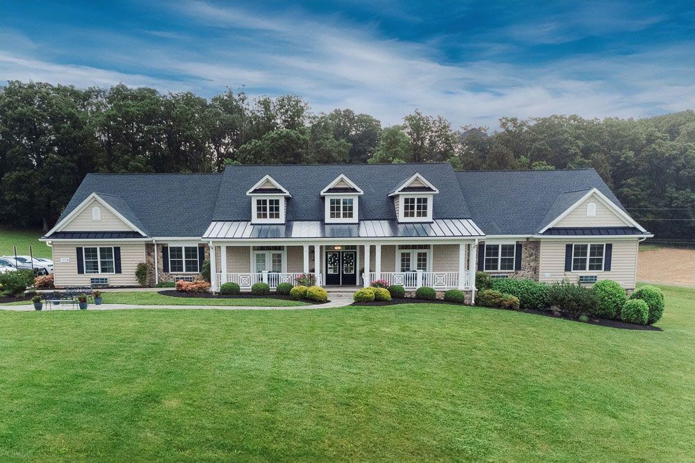 Large beige house with white trim, front porch, and a wide green lawn under a blue sky