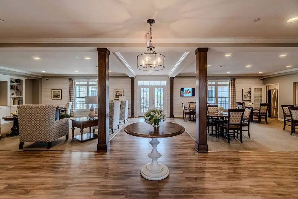 Spacious living room with hardwood floors, chandelier, columns, and seating around a central pedestal table