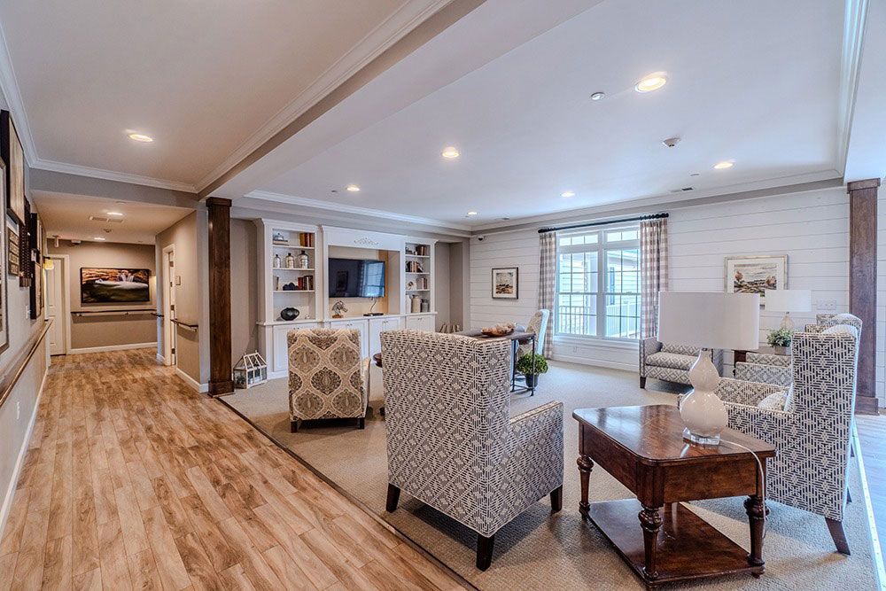 Bright open living room with patterned chairs, wooden floor, and large windows overlooking a patio.