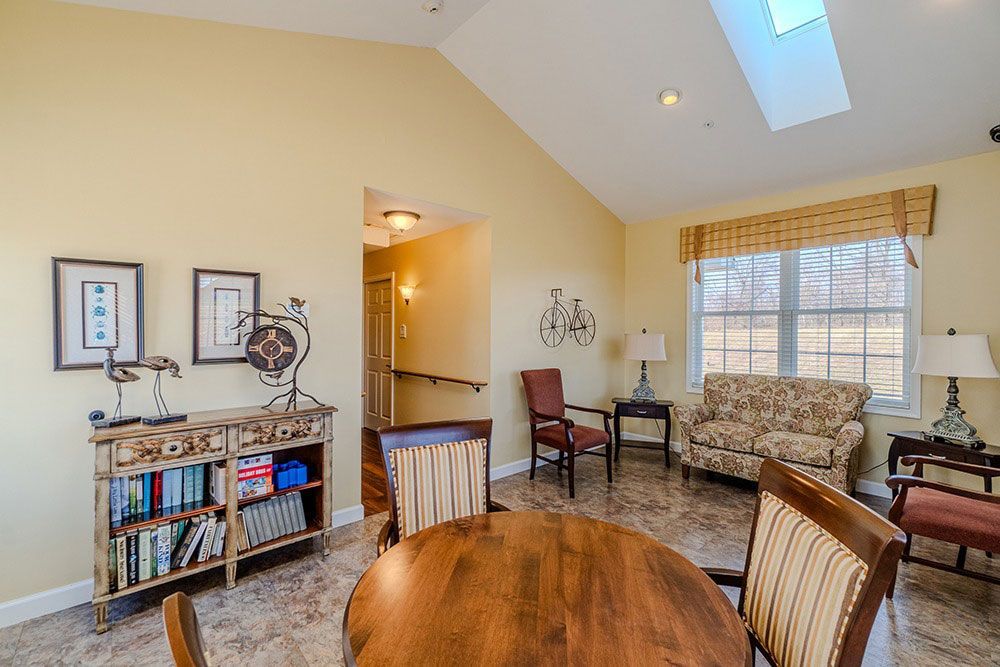 Bright living room with vaulted ceiling, skylight, sofa, chairs, bookshelf, and round wooden table