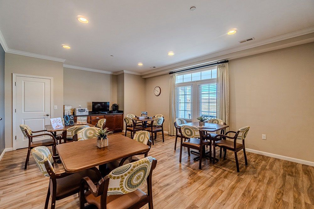 Bright dining room with wooden tables, chairs, recessed lights, and a window with blinds.