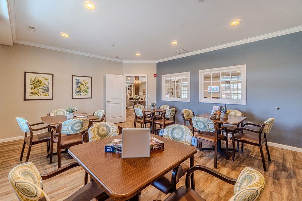 Bright dining room with several tables, wooden chairs, and wall art under recessed ceiling lights.