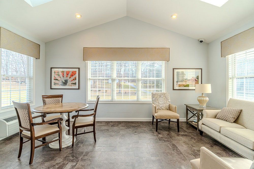 Bright living room with large windows, beige sofa, chairs, round table, and framed wall art