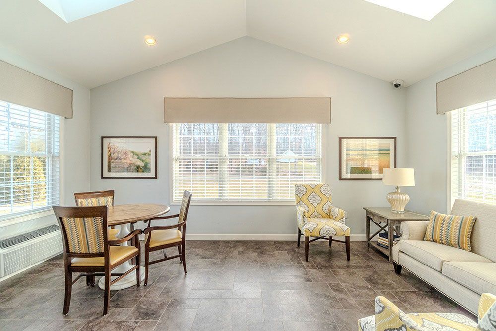 Bright sunroom with white walls, large windows, wood floor, dining table, and beige sofa with chairs