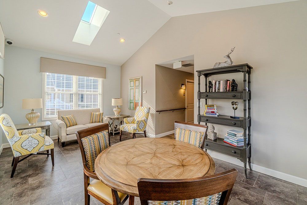 Bright living room with round wooden table, patterned chairs, couch, skylight, and shelving unit