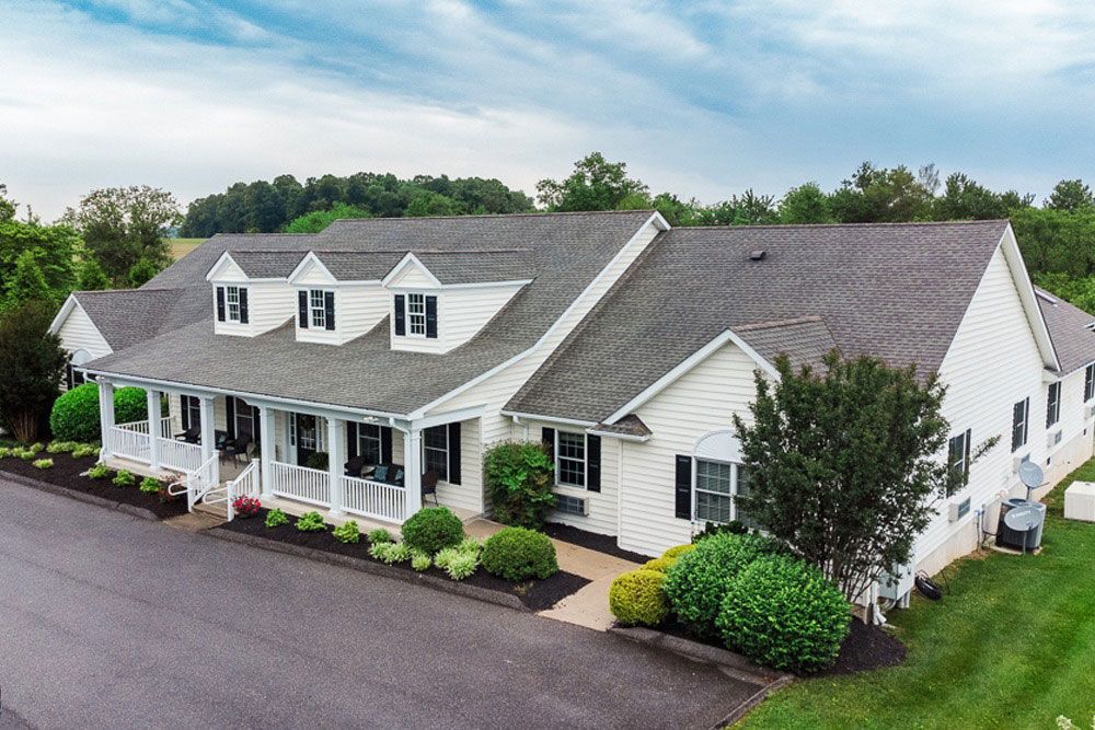 White farmhouse-style home with a front porch, dormer windows, and landscaped yard under a blue sky