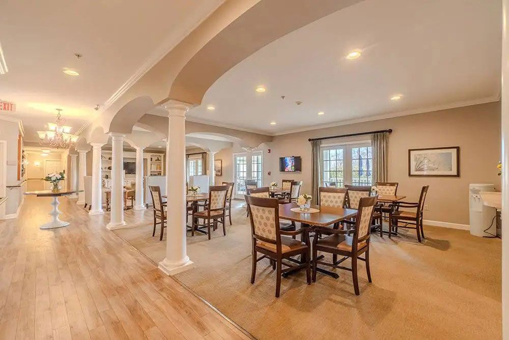Spacious open-plan dining room with wooden floors, white columns, and a set table by large windows