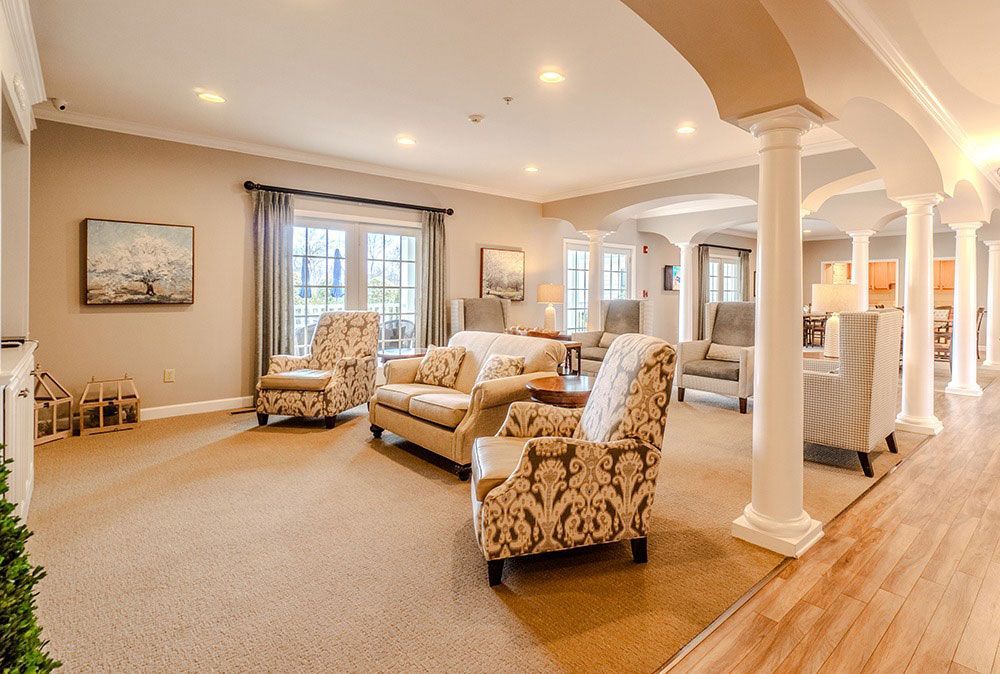 Spacious beige living room with patterned armchairs, sofa, columns, and hardwood floors under recessed lighting