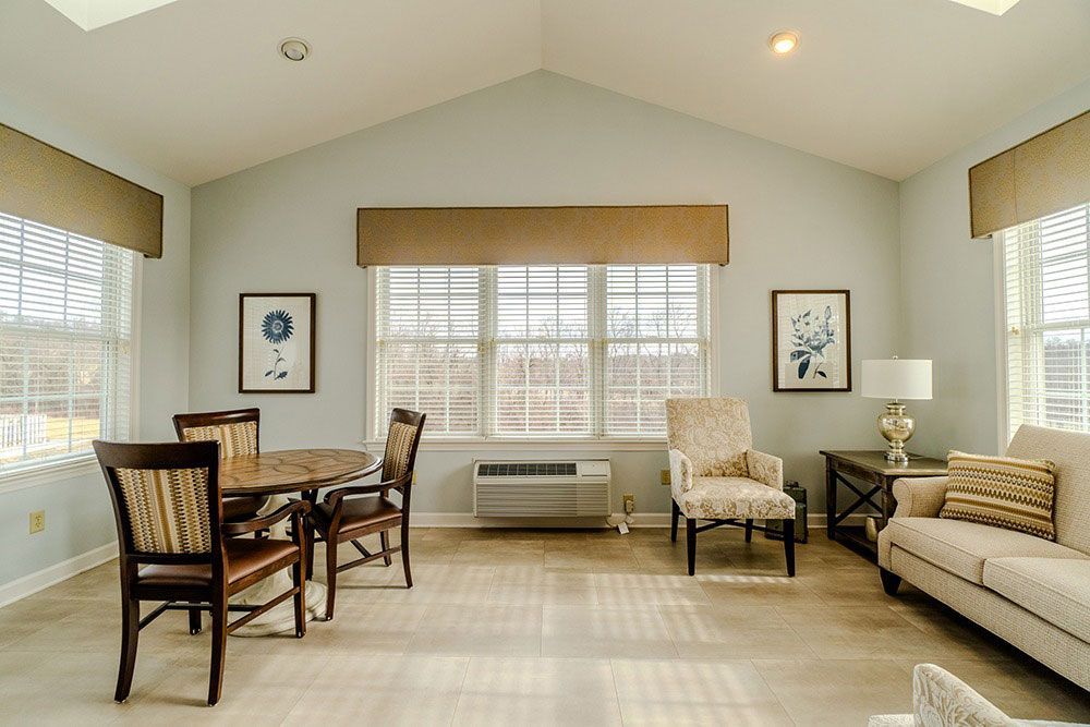 Bright living room with large windows, beige sofa, armchairs, and a glass dining table.