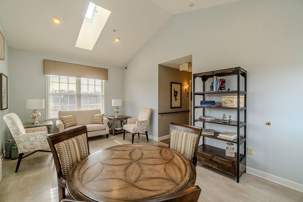 Bright living room with white walls, large windows, wicker chairs, and a round wooden table