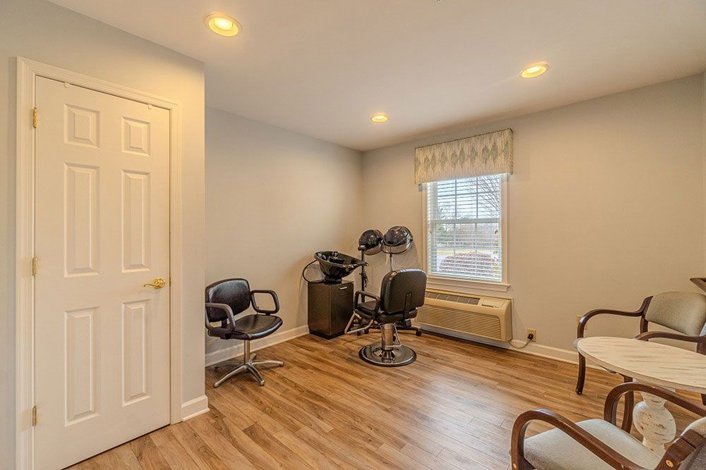 Empty beige room with wood floors, window, chairs, and small table near the wall.