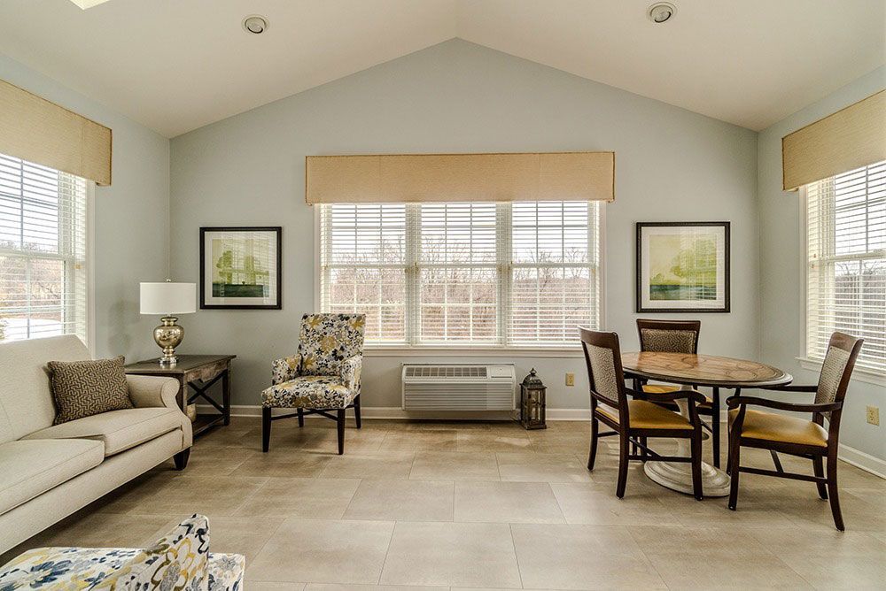 Bright living room with beige sofa, patterned chairs, dining table, and large windows.