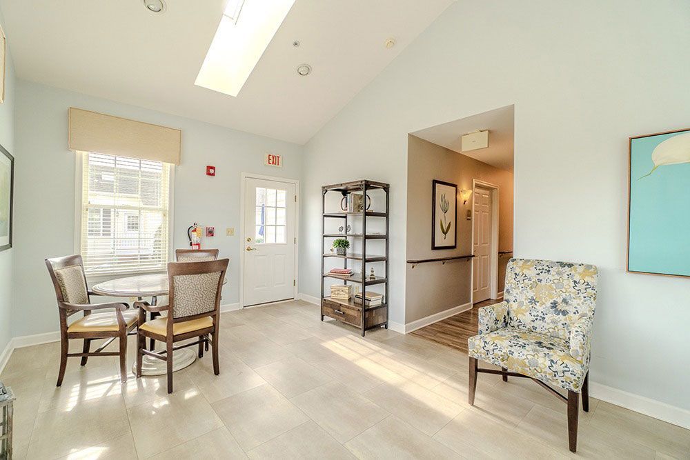 Bright living room with dining table, floral chair, shelving, and sunlit hardwood floors
