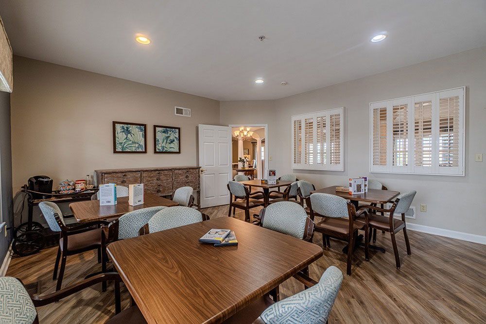 Bright dining room with wooden tables, upholstered chairs, wall art, and window shutters