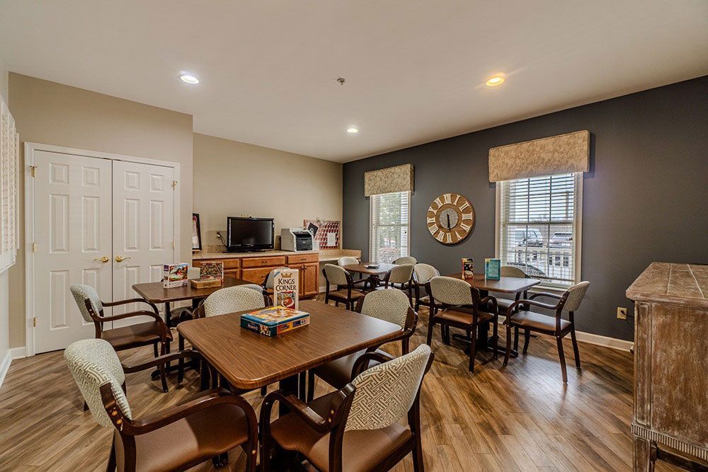 Empty dining room with tables and chairs, wooden floor, and a dark accent wall with a round mirror.