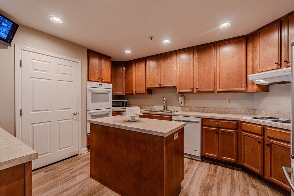 Modern kitchen with wooden cabinets, white appliances, island, and recessed ceiling lights.