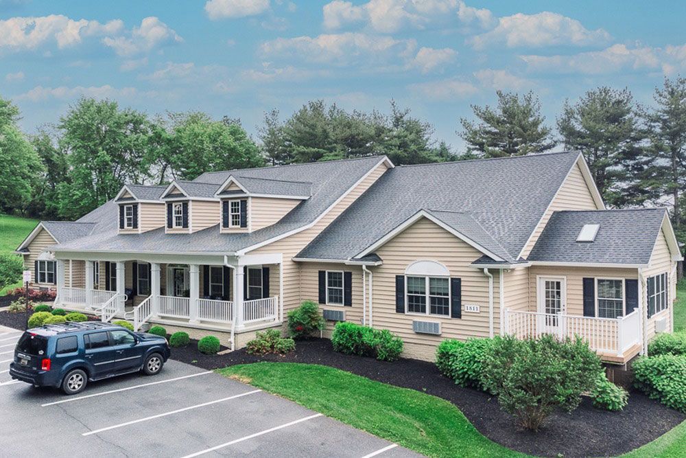 Suburban beige house with gray roof, front porch, and parked SUV under a blue sky