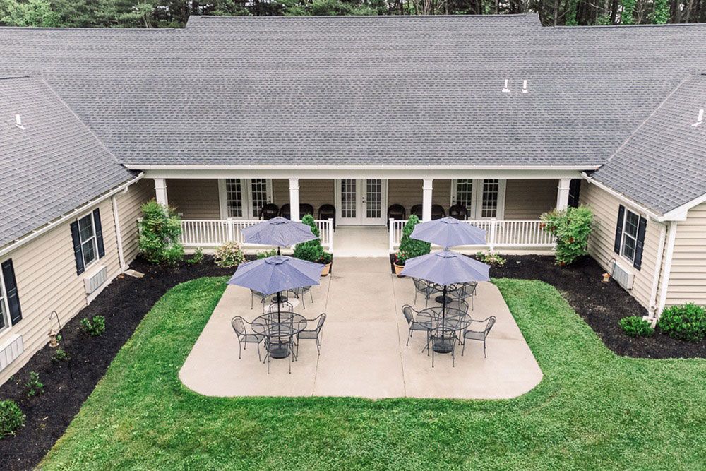 Aerial view of a patio with tables, umbrellas, and chairs beside a large house and lawn