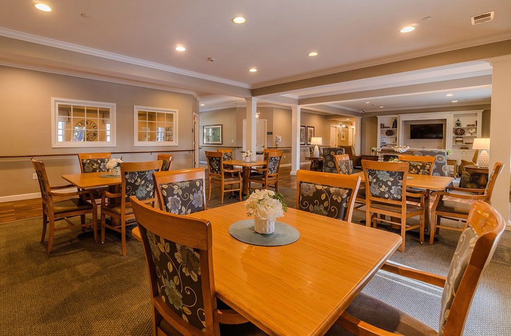 Bright dining room with wooden tables and chairs, warm recessed lighting, and a buffet in the background