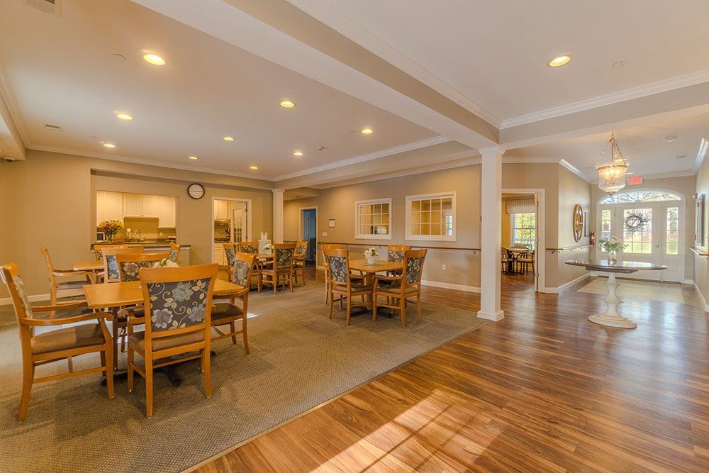 Spacious dining room with tables, chairs, and warm recessed lighting, opening to a bright lobby area