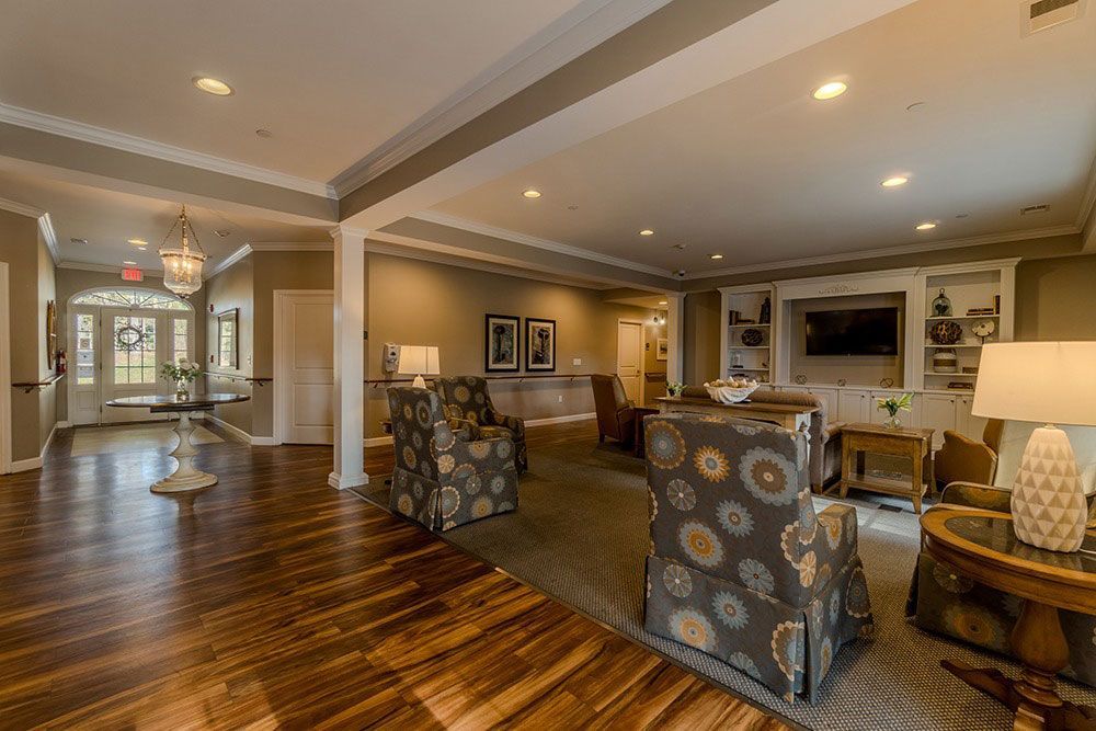 Spacious elegant living room with hardwood floors, patterned chairs, recessed lighting, and a fireplace
