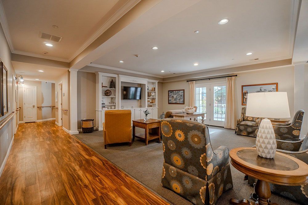 Bright living room with wood floors, patterned chairs, lamp, sofa, and French doors to a patio.