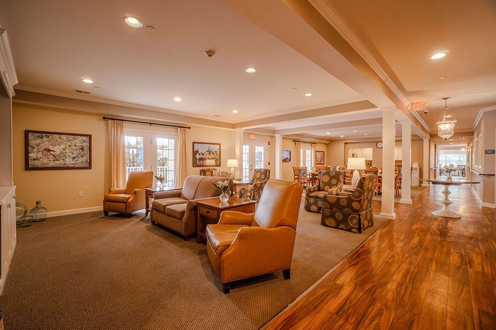 Spacious living room with tan chairs, stone fireplace, hardwood floor, and recessed ceiling lights