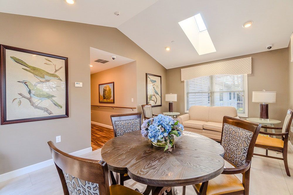 Bright dining area with round table, wicker chairs, beige sofa, and skylight under vaulted ceiling