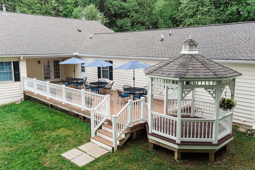 Backyard deck with white railing, patio furniture, and a white gazebo beside a house and green lawn