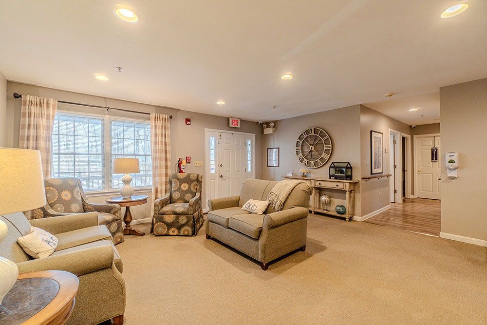 Bright living room with beige furniture, large windows, recessed lighting, and a hallway in the background